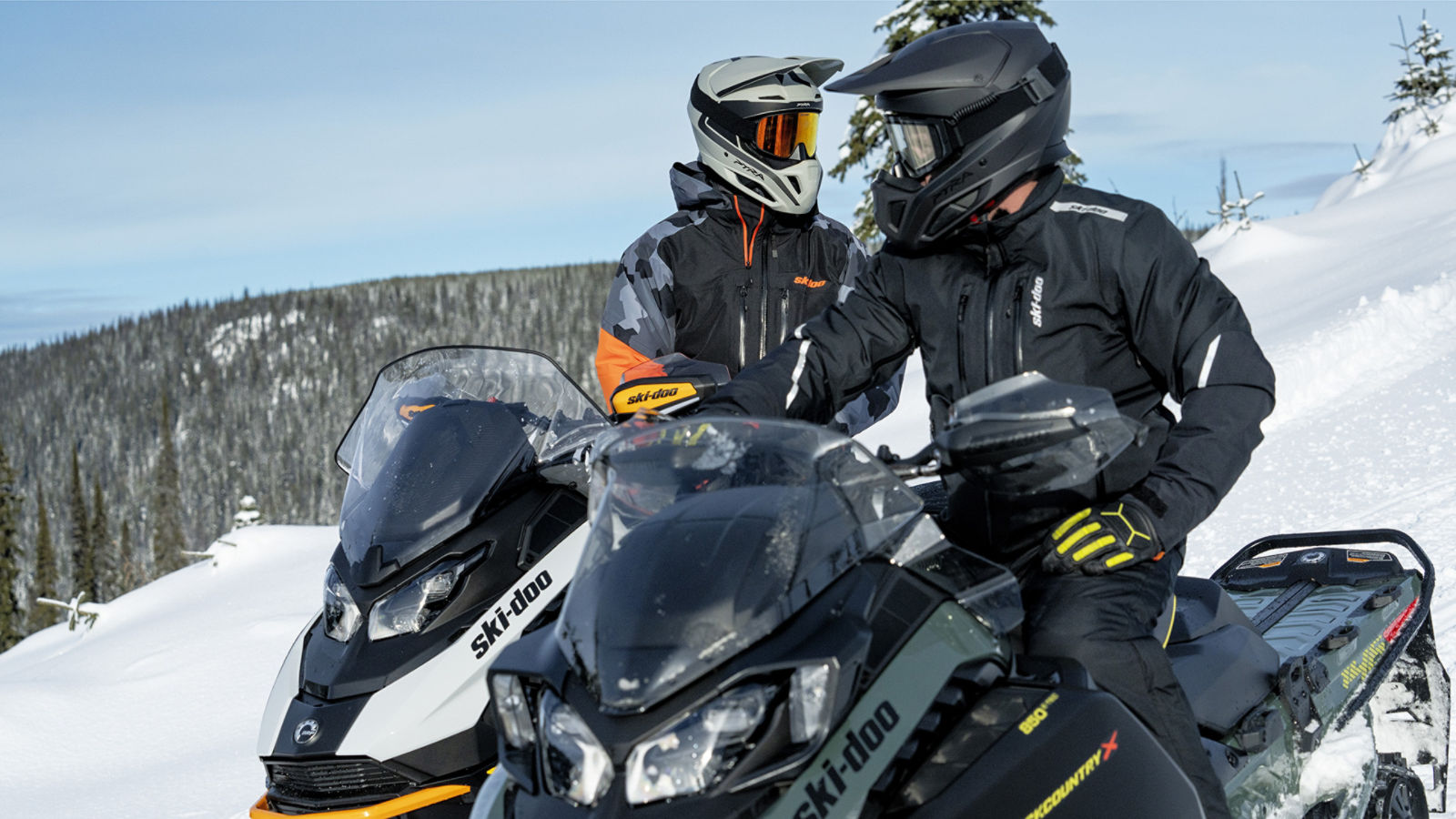 Two riders on thei Ski-Doo snowmobile, idle, on top of a hill
