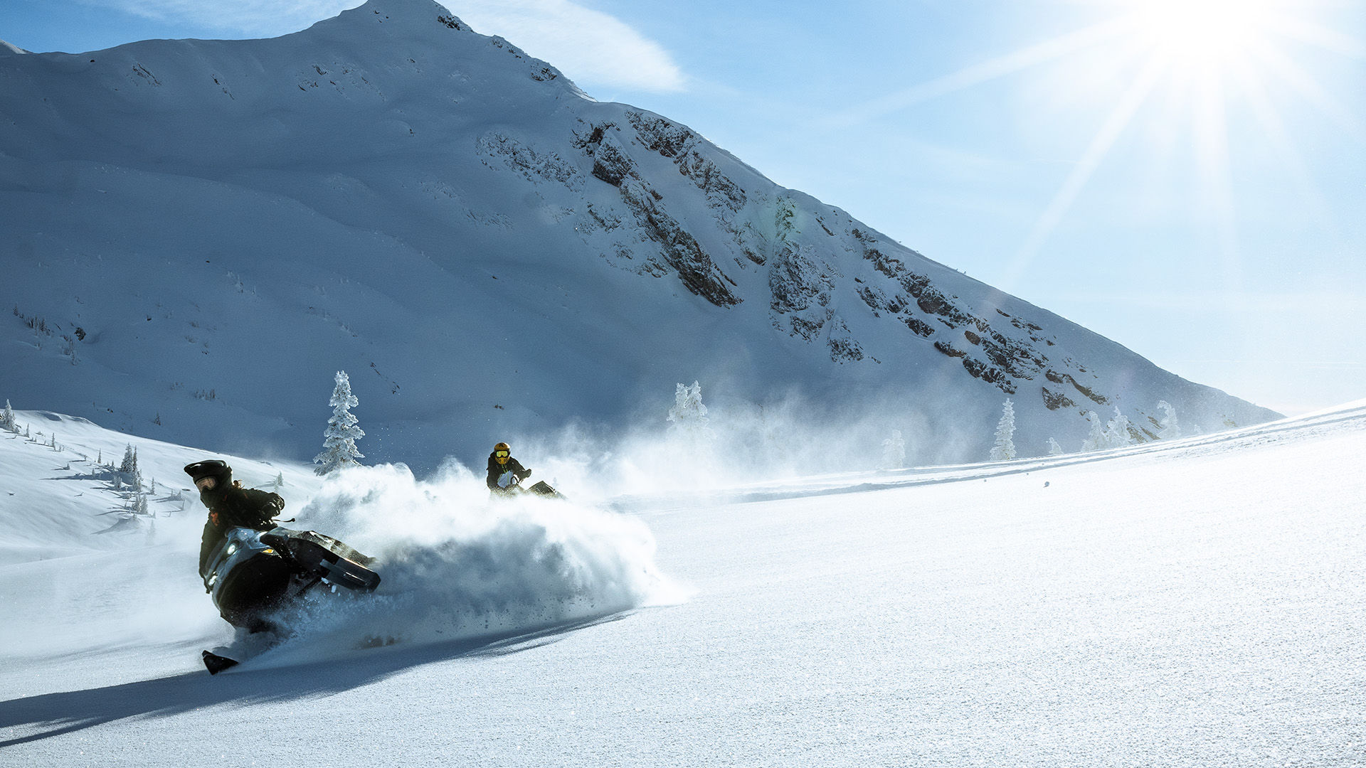 Two snowmobilers riding their 2026 Ski-Doo snowmobiles through the deep snow of the mountain.