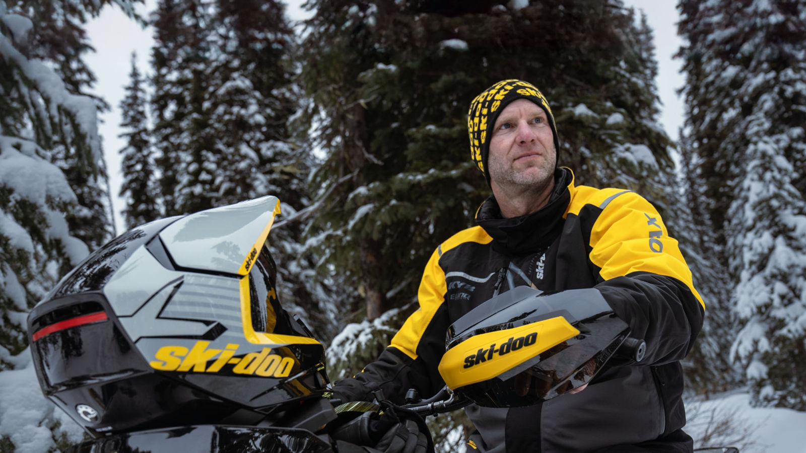 A man sitting on a snowmobile wearing Ski-Doo riding gear.
