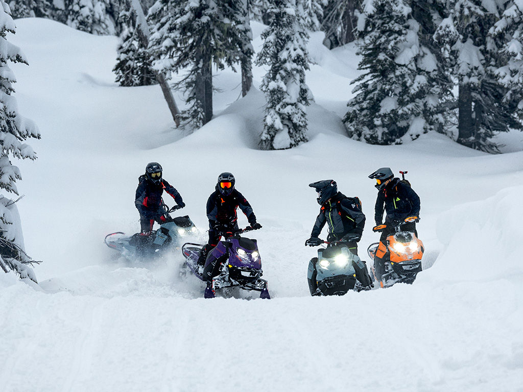 Four riders taking a break from riding in the middle of a snowy hill on their 2027 Ski-Doo snowmobiles
