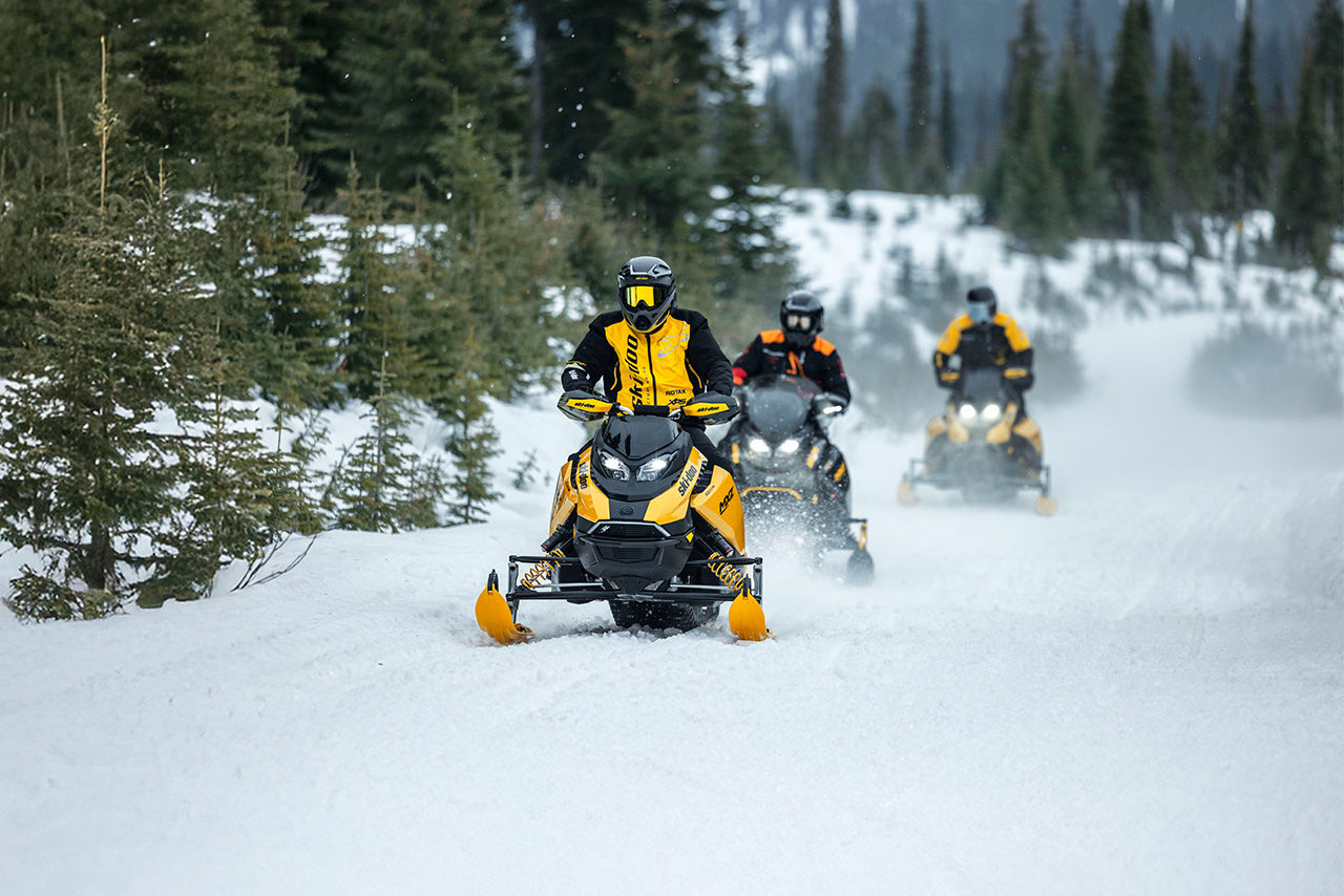 Three riders  riding in the middle of a snowy hill on their 2027 Ski-Doo snowmobiles
