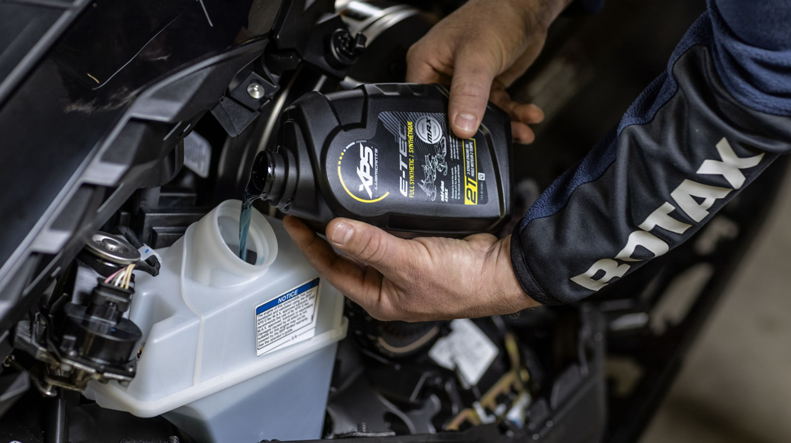 Rider pourring E-TEC synthetic oil on a Lynx snowmobile
