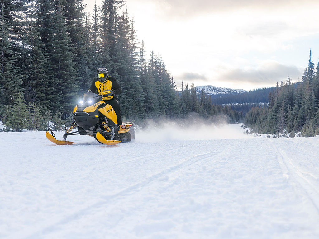 Rider riding a 2027 Ski-Doo MXZ X-RS in a snowy field surrounded by trees