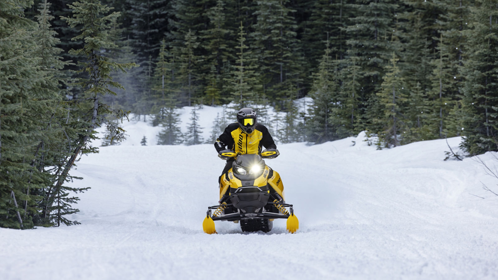 Rider going at high speed with a 2027 Ski-Doo MXZ RS snowmobile on a snowy trail surrounded by trees