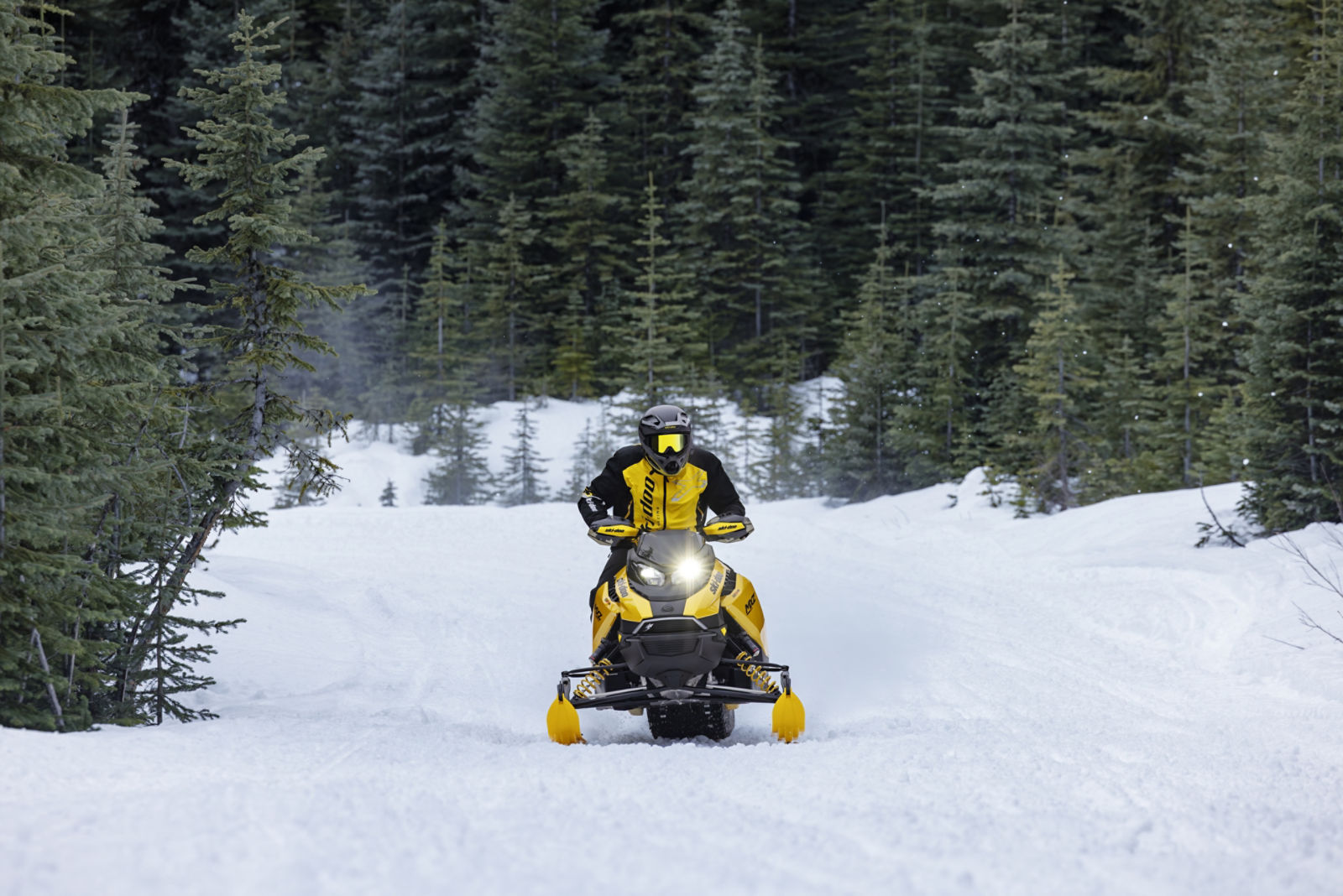 Rider going at high speed with a 2027 Ski-Doo MXZ RS snowmobile on a snowy trail surrounded by trees