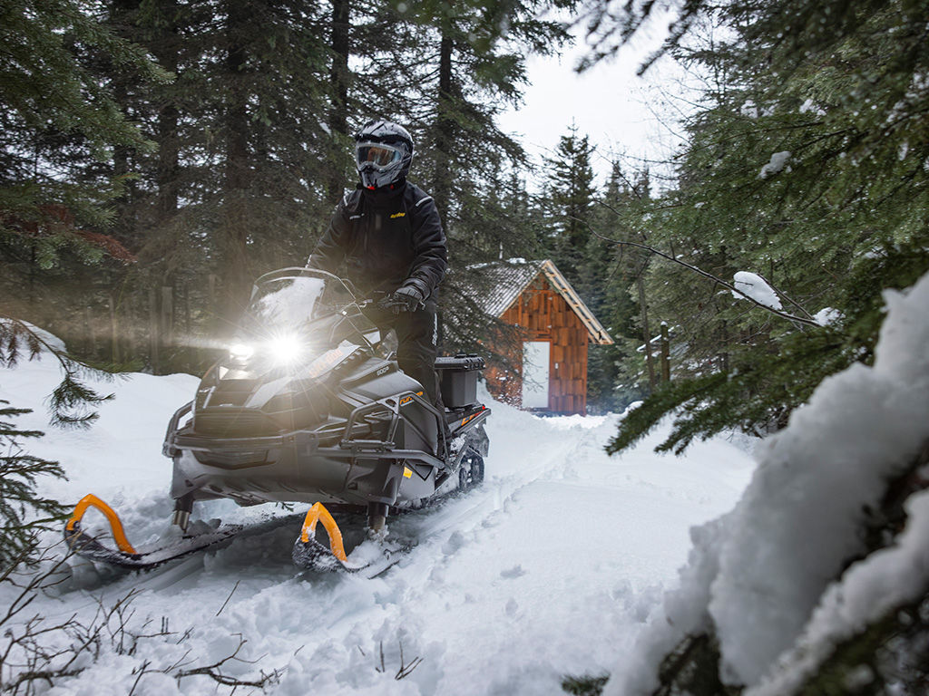 Motoneigiste qui quitte son chalet avec une motoneige Ski-Doo Tundra LE 2027 dans une forêt enneigée