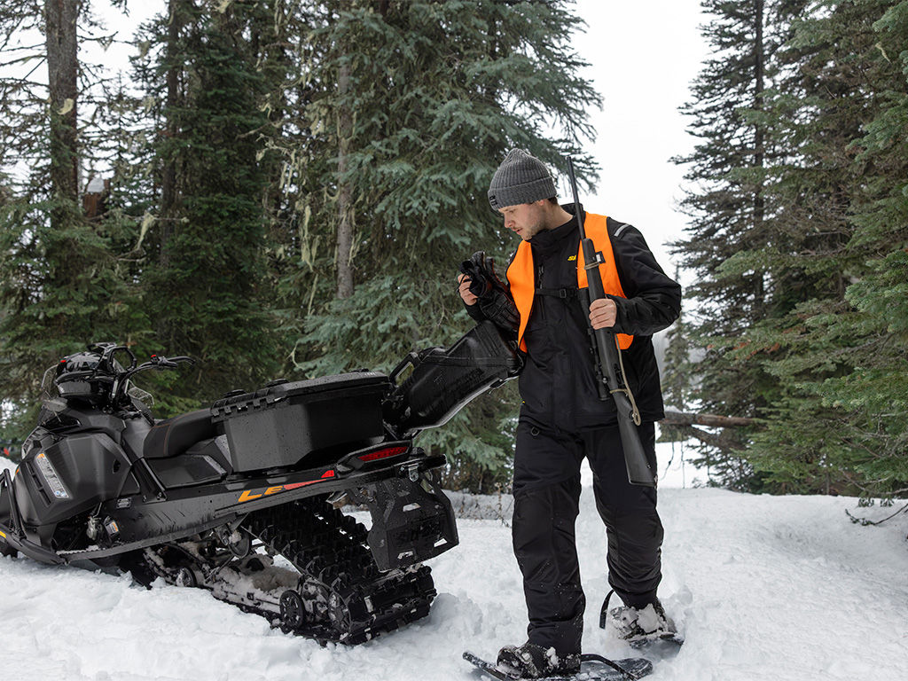 Rider, next to his 2027 Ski-Doo Tundra LE, about to go snowshoeing with a rifle