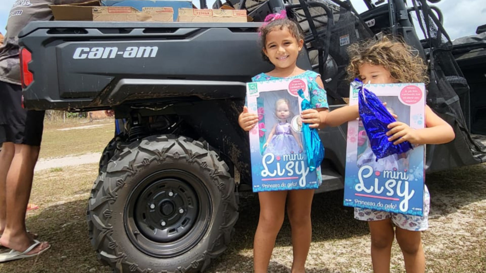 Dos niñas pequeñas con juguetes infantiles junto a un Can-Am.
