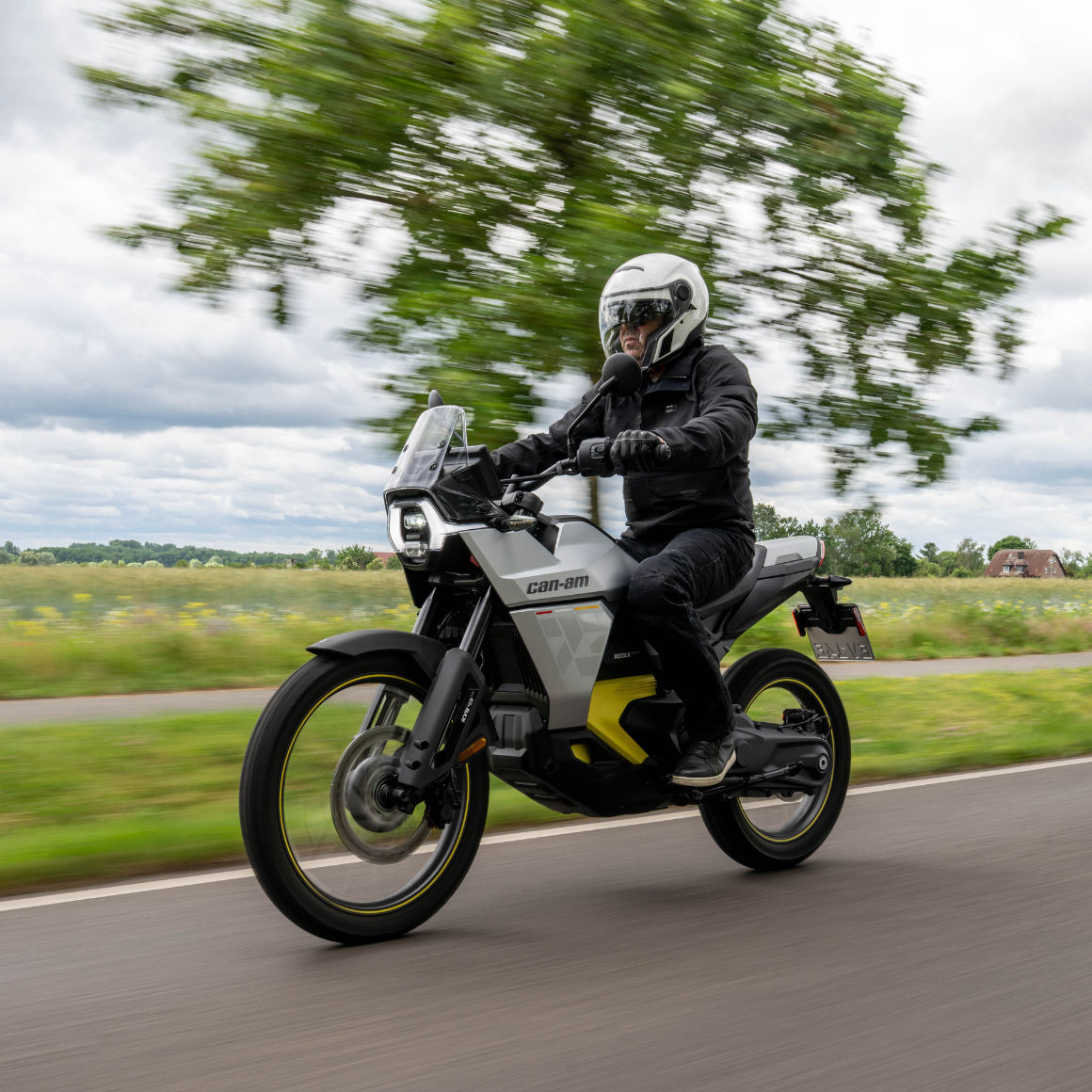 Man riding a Can-Am Origin electric motorcycle next to a field
