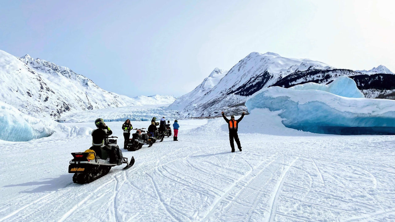 Un homme faisant la fête devant un glacier avec sa motoneige