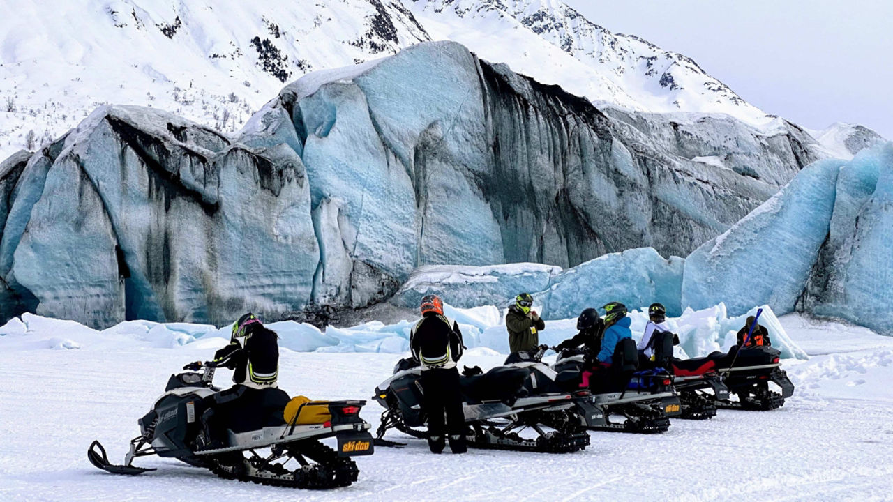 Un homme faisant la fête devant un glacier avec sa motoneige