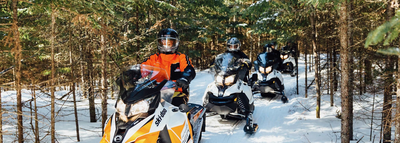 Un groupe de personnes roulant en Ski-Doo dans un sentier.