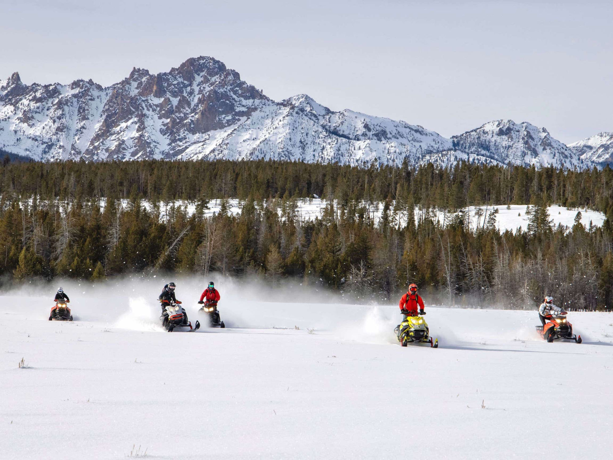 Crew of snowmobilers riding in front of mountains