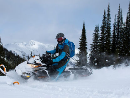 Snowmobiler turning in the snow with mountains in the background