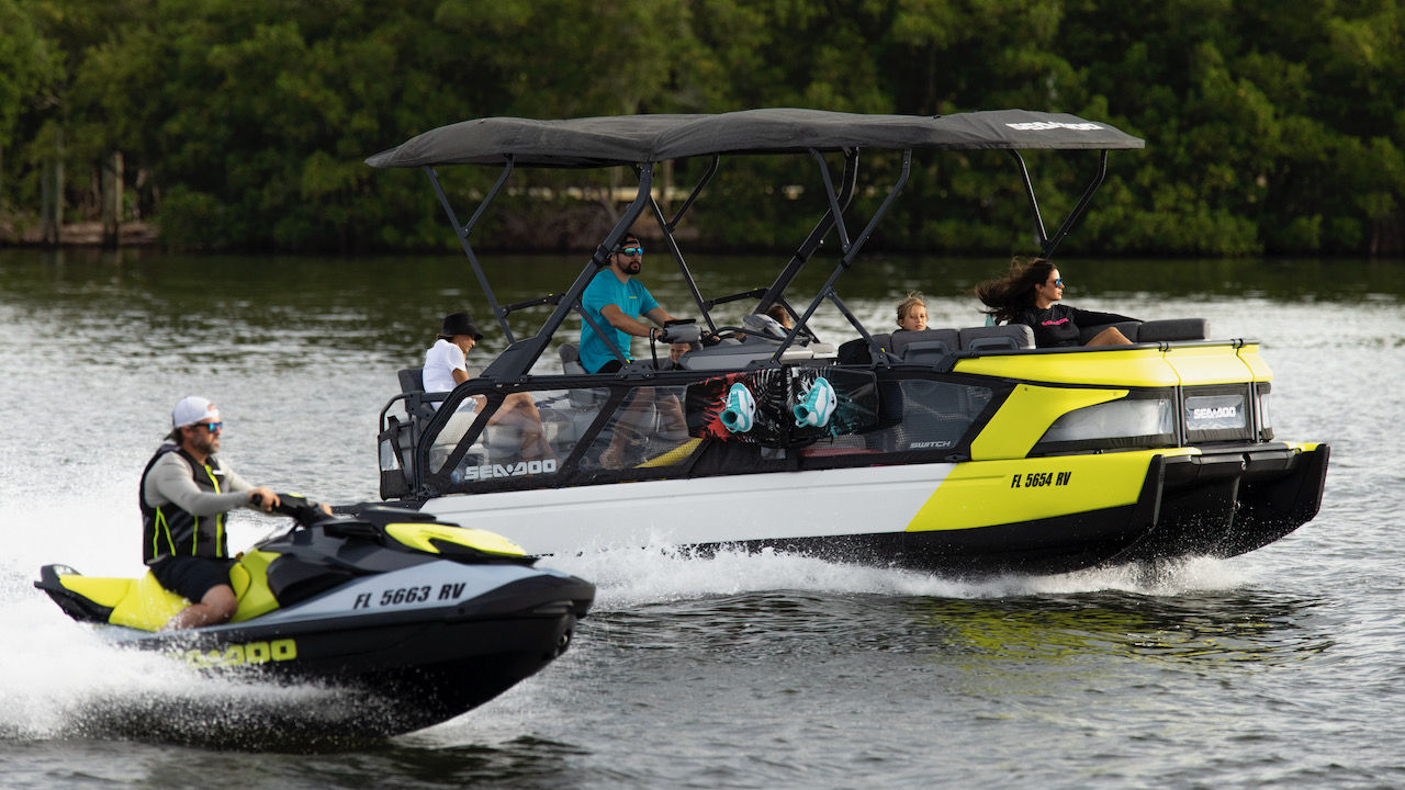 Une famille à bord d'un ponton Sea-Doo Switch à côté d'un homme sur une motomarine Sea-Doo, tous deux naviguant sur le lac