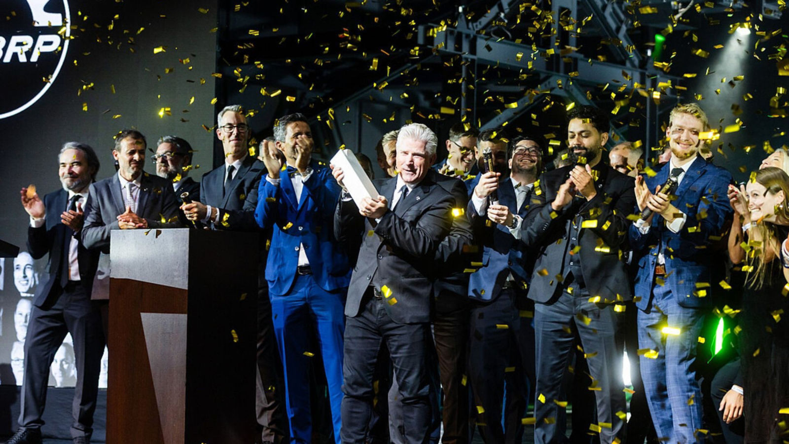 BRP team on stage celebrating at the Red Dot Award ceremony as gold confetti falls and an award is held up.